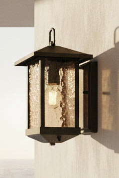 A matt black outdoor wall-mounted light fixture with a water glass cover and a hanging loop on the top.