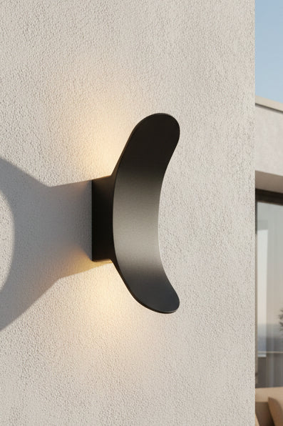 A matte black up and down light fixture mounted on a wall, partially illuminated, providing a warm light.