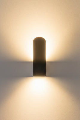 A matte black wall-mounted LED light fixture with an illuminated section on a orange wall.