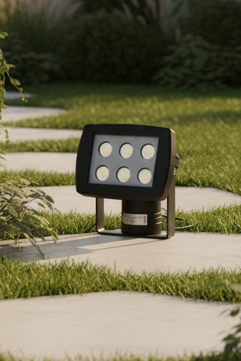 An outdoor spike light with LED bulbs, in a matt black finish, placed on a grass-like surface.