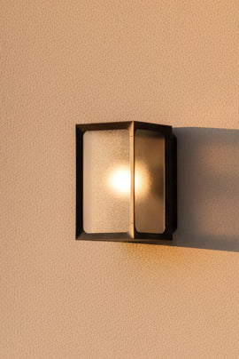 Black outdoor wall washer with a frosted glass cover and a warm light visible inside.